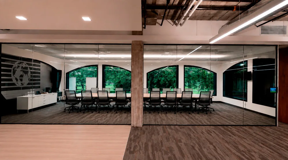 An office partition with PriWatt PDLC film on the existing glazing, clear — the boardroom, arched windows and trees behind it